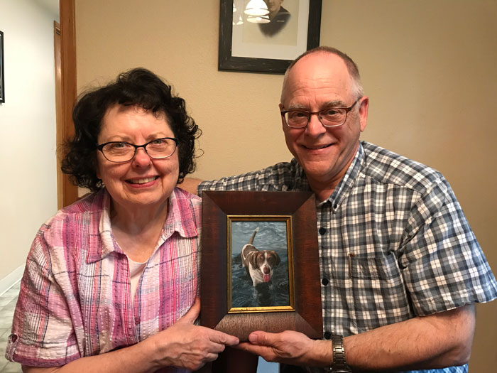 couple posing with their commissioned pet portrait, a gift from their daughter, painted by Rebecca Luncan