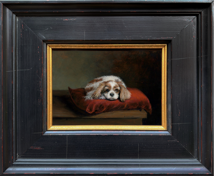Framed Oil painting of a Blenheim Cavalier King Charles Spaniel named Betty, posed on a red velvet cushion atop a wooden table with a dark background by Rebecca Luncan